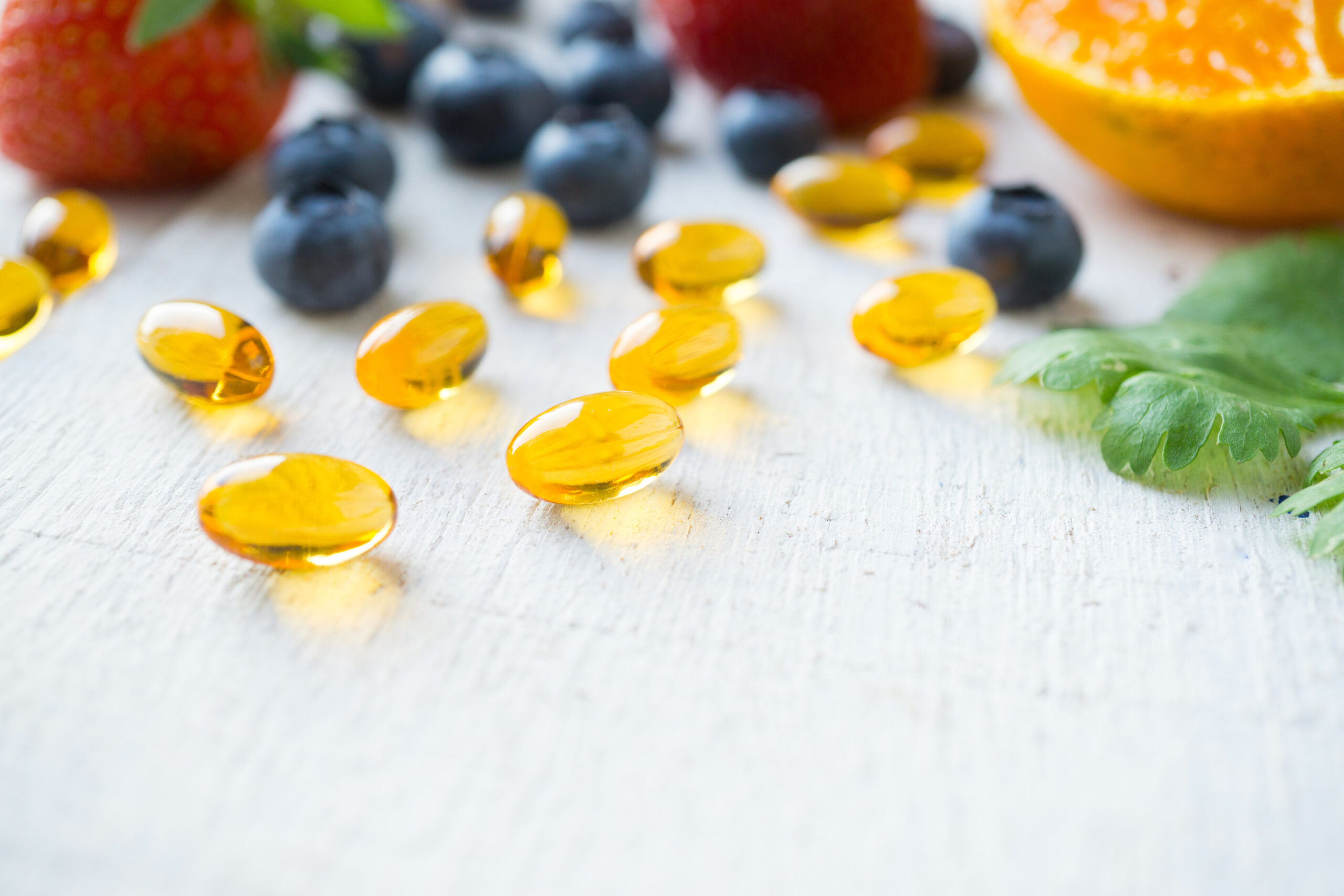 Close up vitamin supplement with healthy fruits blueberry, strawberry, and orange on white wood background.