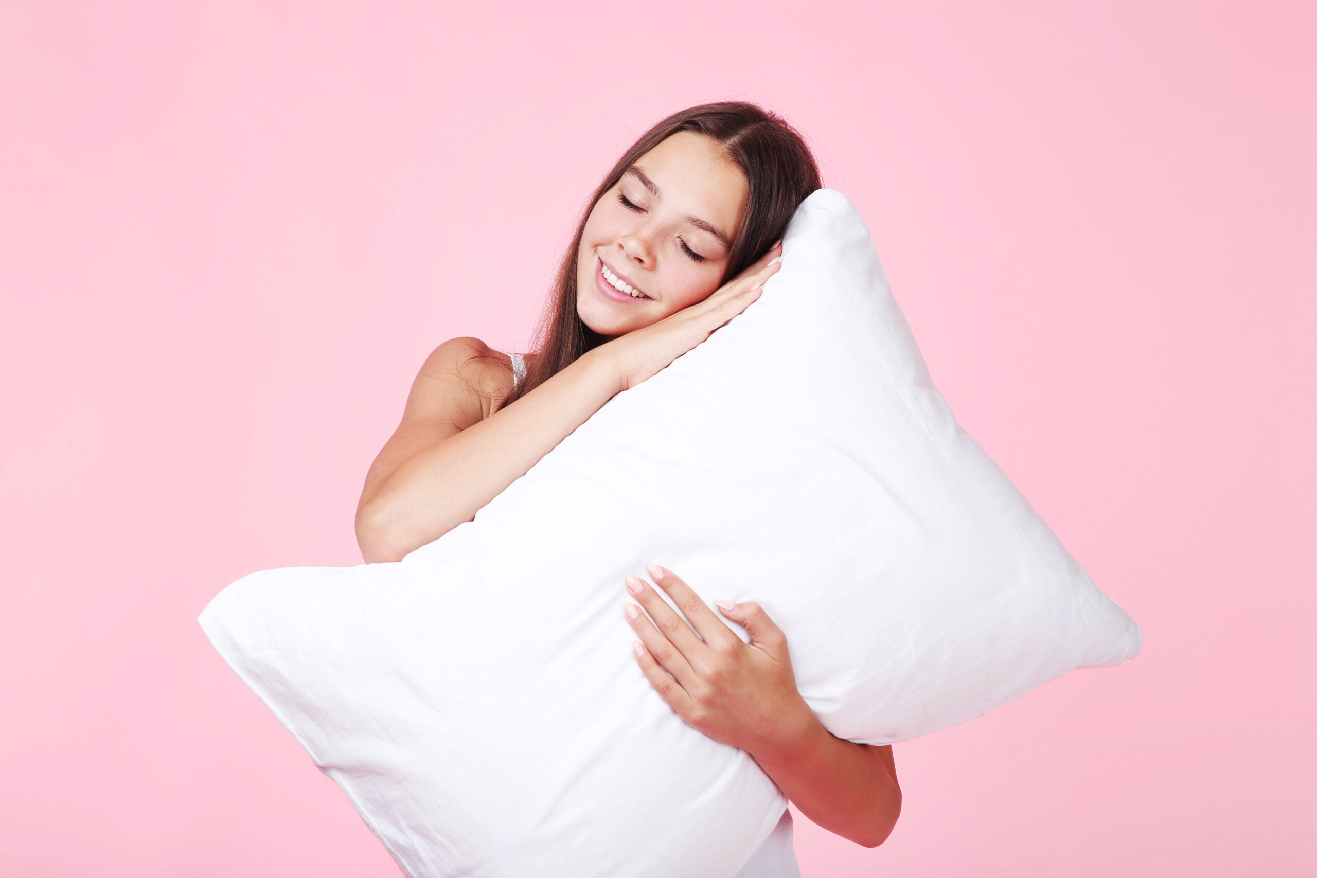 Young girl with white pillow on pink background