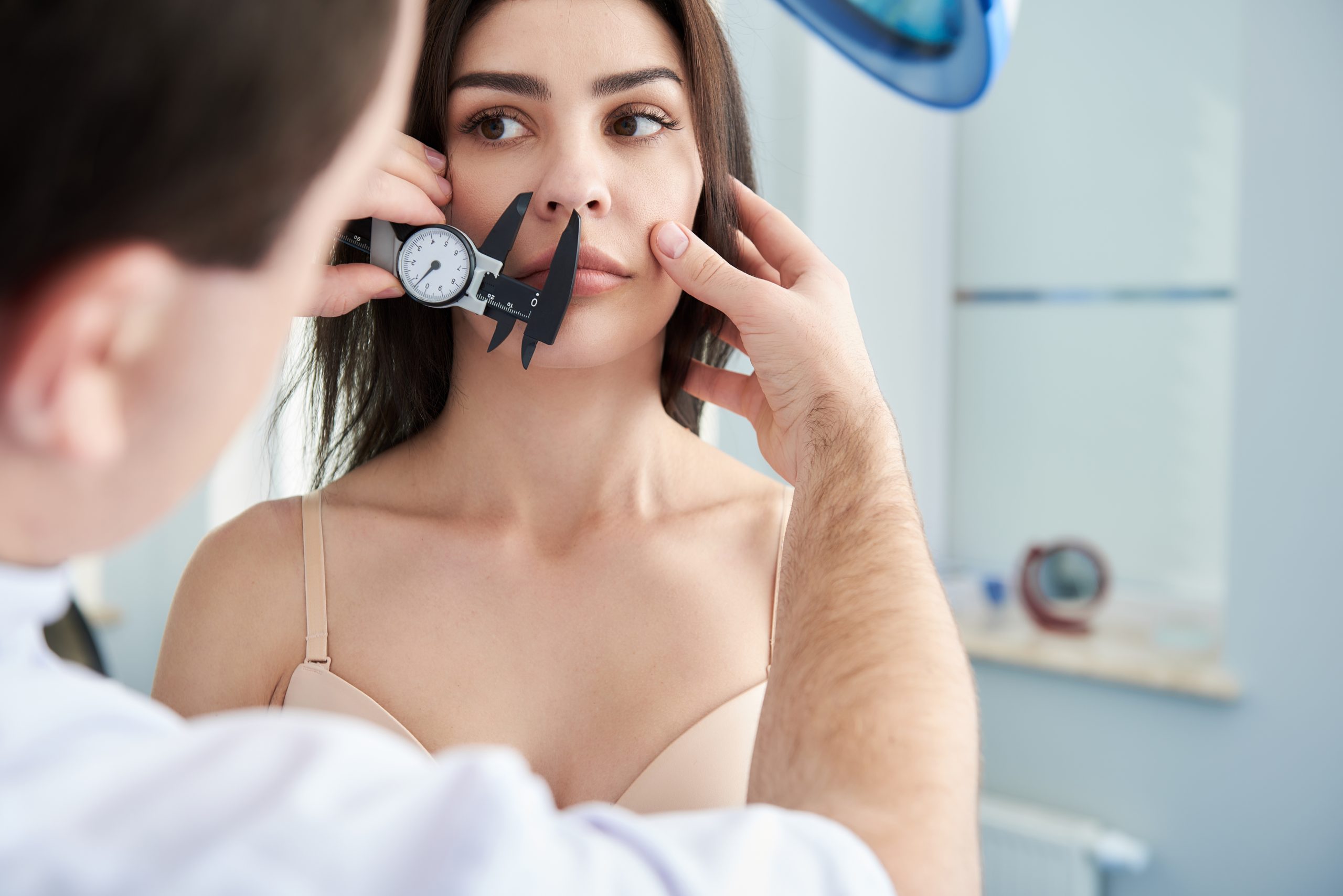 Doctor measuring face of female patient with calipers